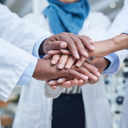 Shot of a group of unrecognisable scientists joining hands in solidarity in a laboratory.